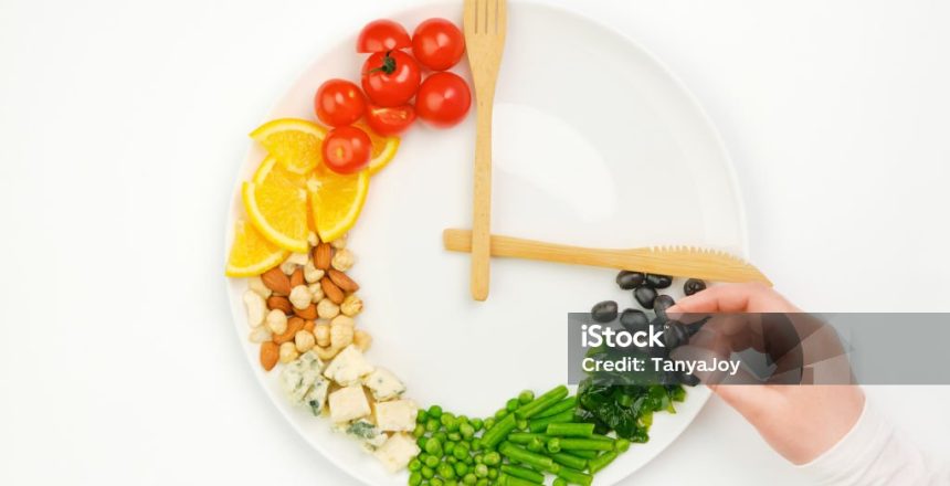 Colorful food and cutlery arranged in the form of a clock on a plate. Olive in hand. Intermittent fasting, diet, weight loss, lunch time concept.